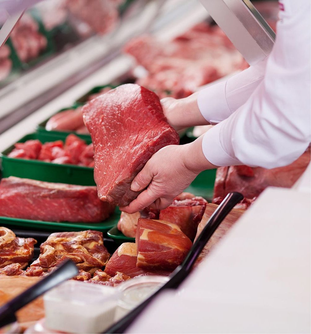 Ein Metzger hält ein Stück Fleisch in der Frischetheke